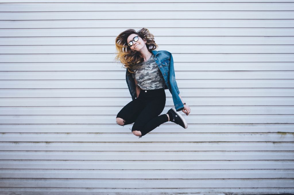 A girl jumps in front of a white wall.