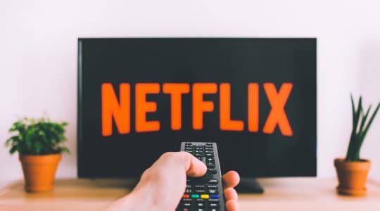Hand holding a TV remote in front of a Netflix screen